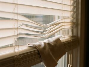 Beschadigde witte jaloezieën met gebogen lamellen en schoonmaakdoek, close-up met natuurlijk zonlicht