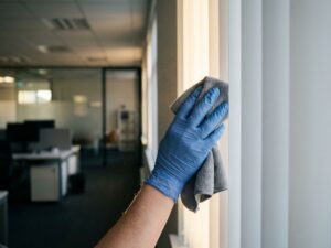 Schoonmaakspecialist reinigt witte verticale jaloezieën met microvezeldoek in modern kantoor