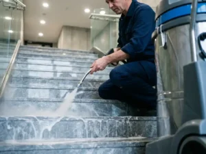 Professionele schoonmaker reinigt marmeren trappen met hogedruкstoomreiniger in modern appartementengebouw, zeepsop op gepolijste steen.