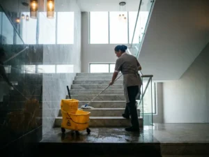 Professionele schoonmaker in uniform die marmeren trappenhuis dweilt in modern appartementengebouw, met glanzende treden en natuurlijk licht.